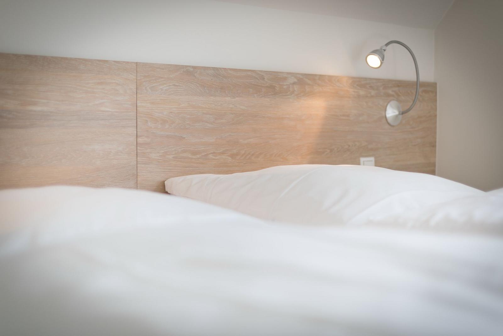 Wooden headboard with wall lamp and white bedding.
