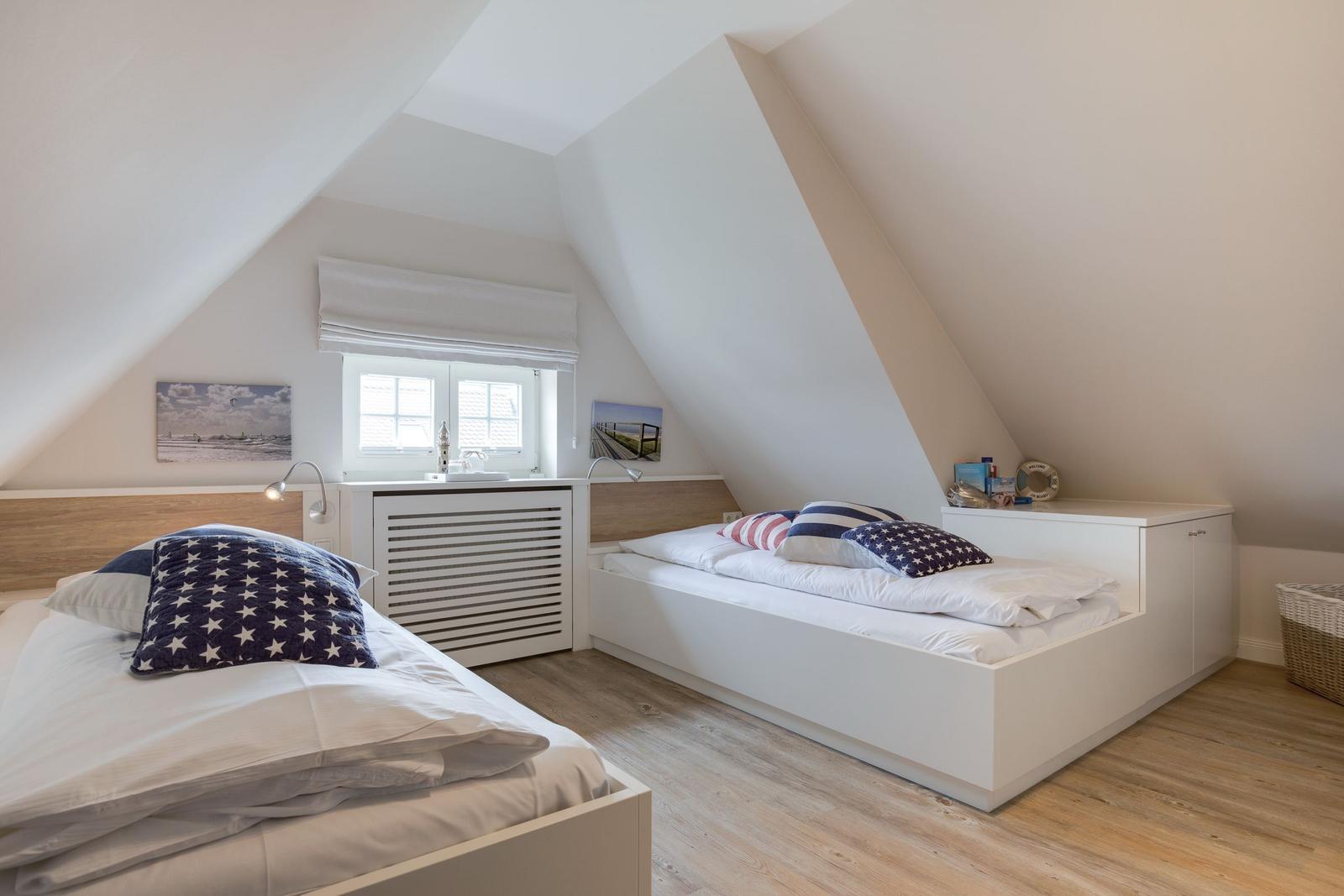 Room with two beds, sloped ceilings, and window with roller blind.
