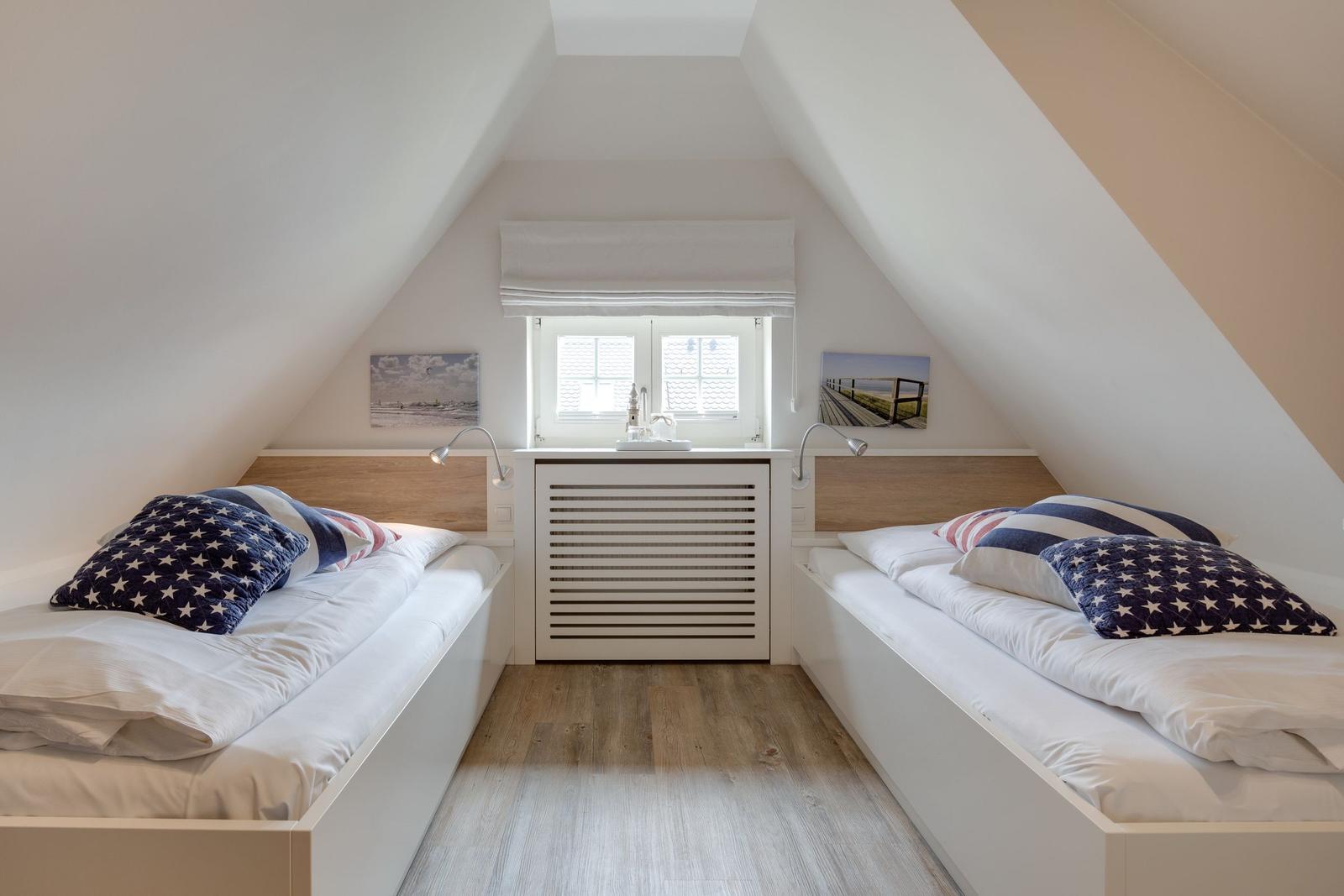 Two single beds under sloped ceilings with window and wooden floor