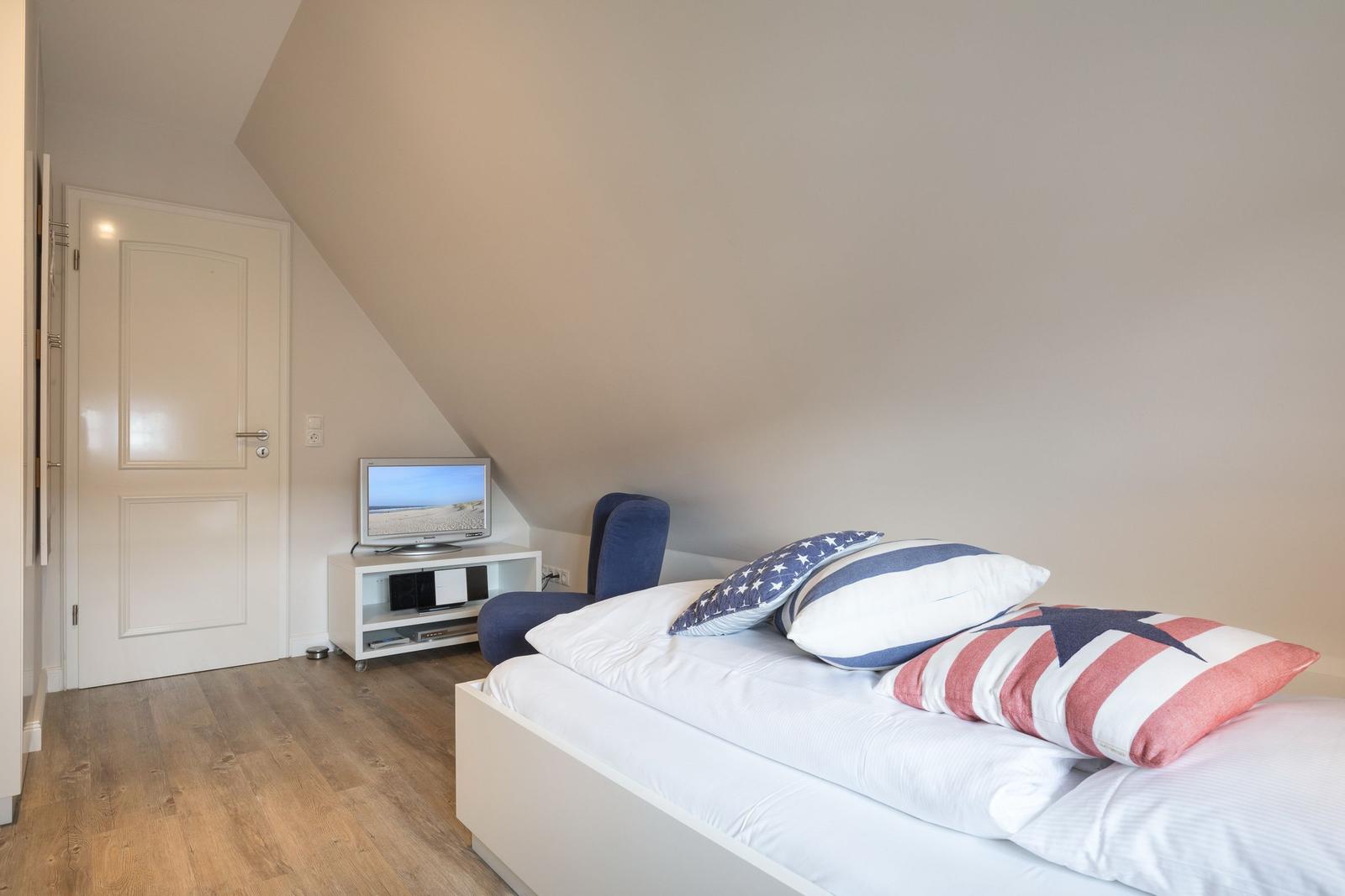Bedroom with bed, TV, and chair under sloped ceiling.