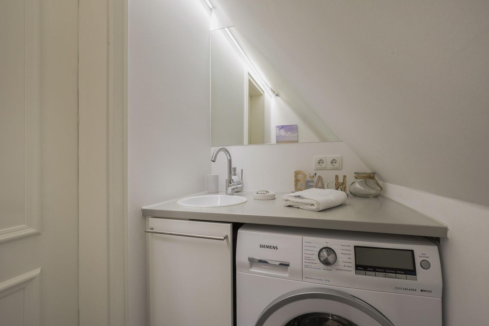 Washing machine and sink under sloped ceiling with mirror and towel.