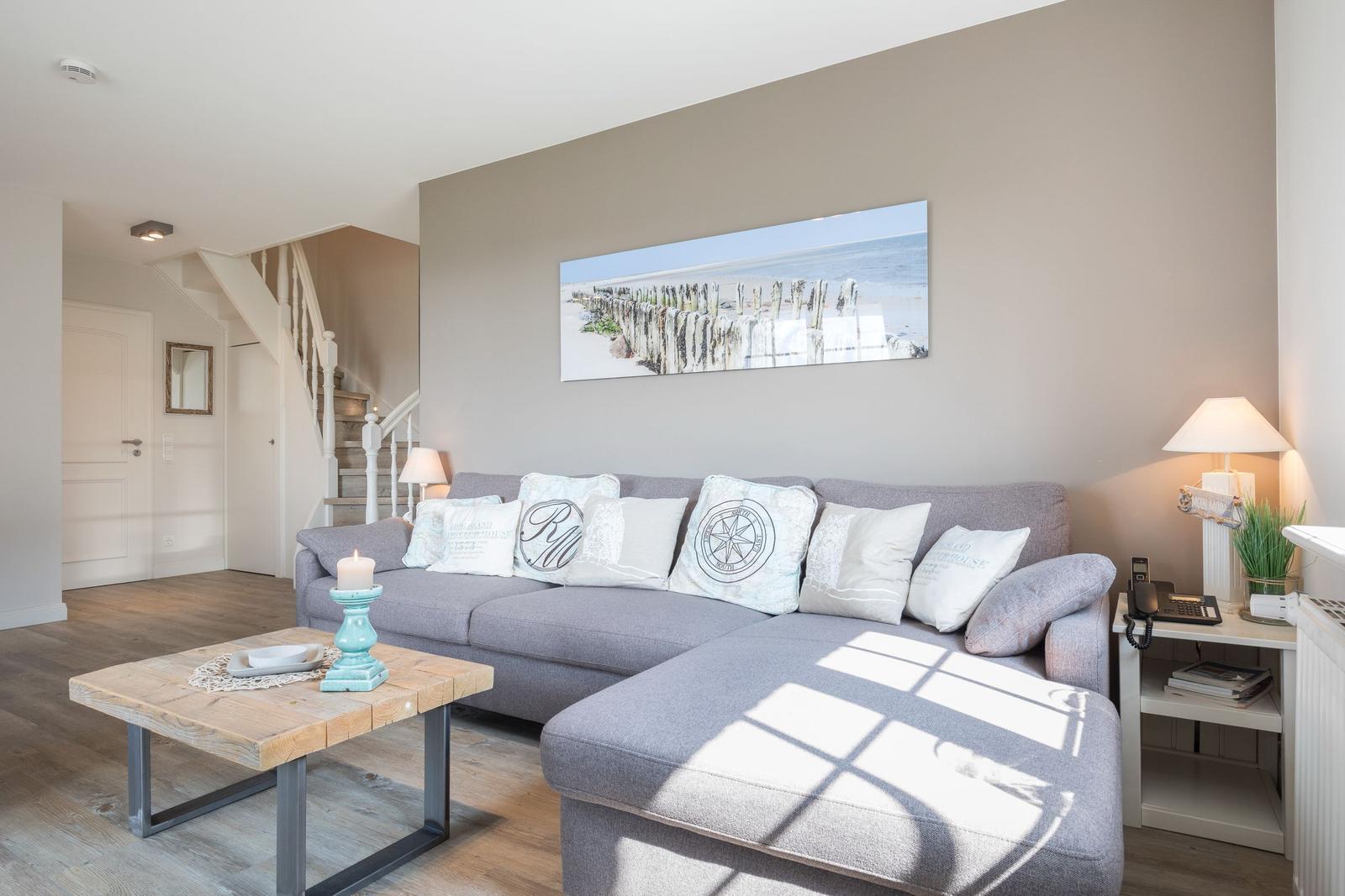 Living room with gray sofa, wooden table, and wall art. Staircase in background.