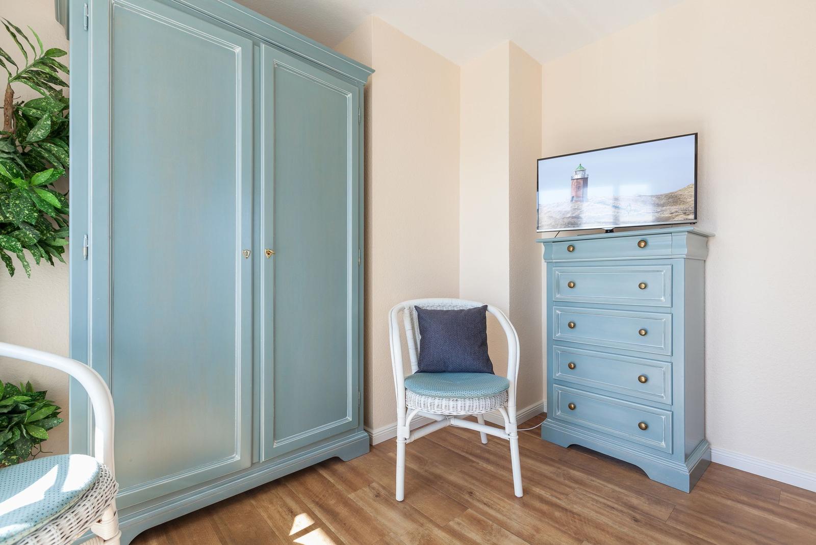 Schlafzimmer mit Kleiderschrank, Stuhl und TV auf Kommode.