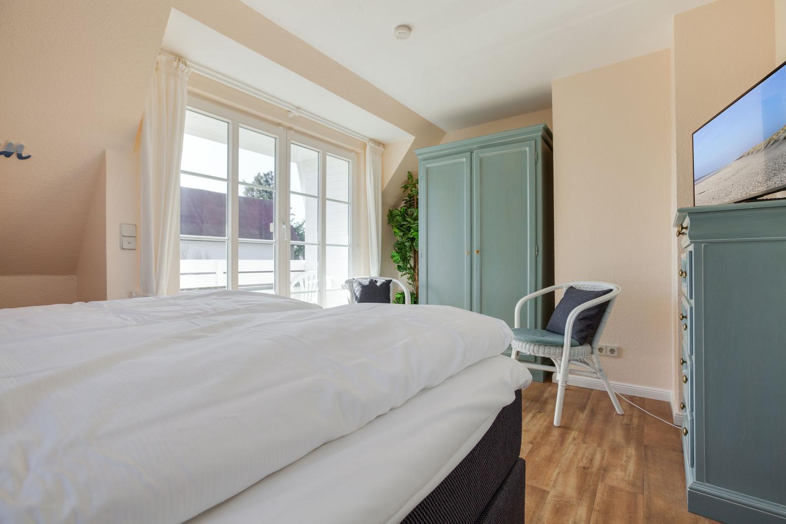 Schlafzimmer mit Doppelbett, Fenster, Kleiderschrank und Fernseher.