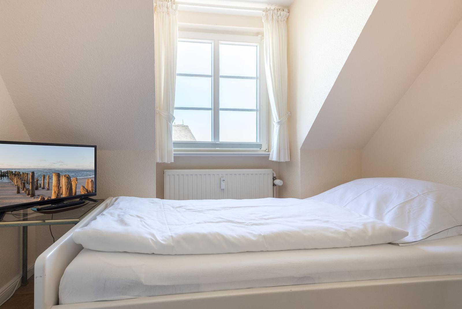 Schlafzimmer mit Dachfenster, Bett und Fernseher.