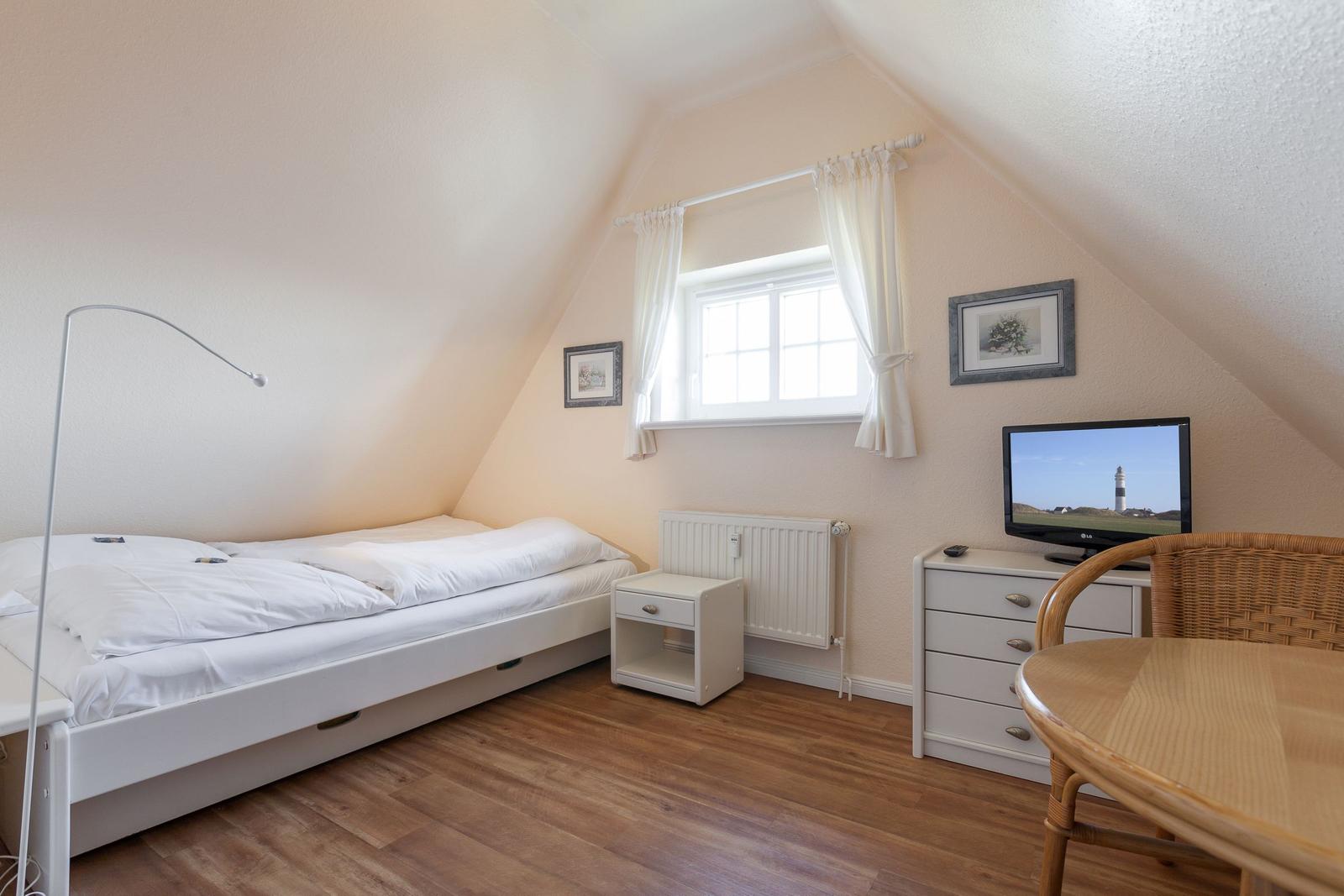 Schlafzimmer mit Dachschräge, Bett, TV und Schreibtisch.