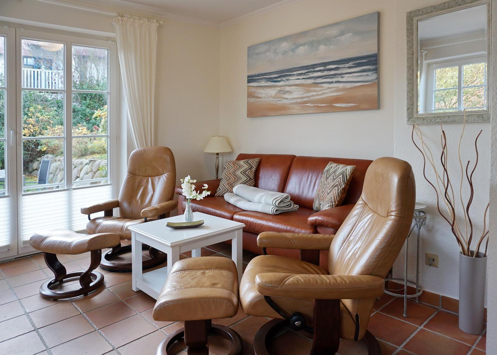 Wohnzimmer mit Ledersofa und zwei Sessel, großes Fenster, Wandbild und Spiegel.