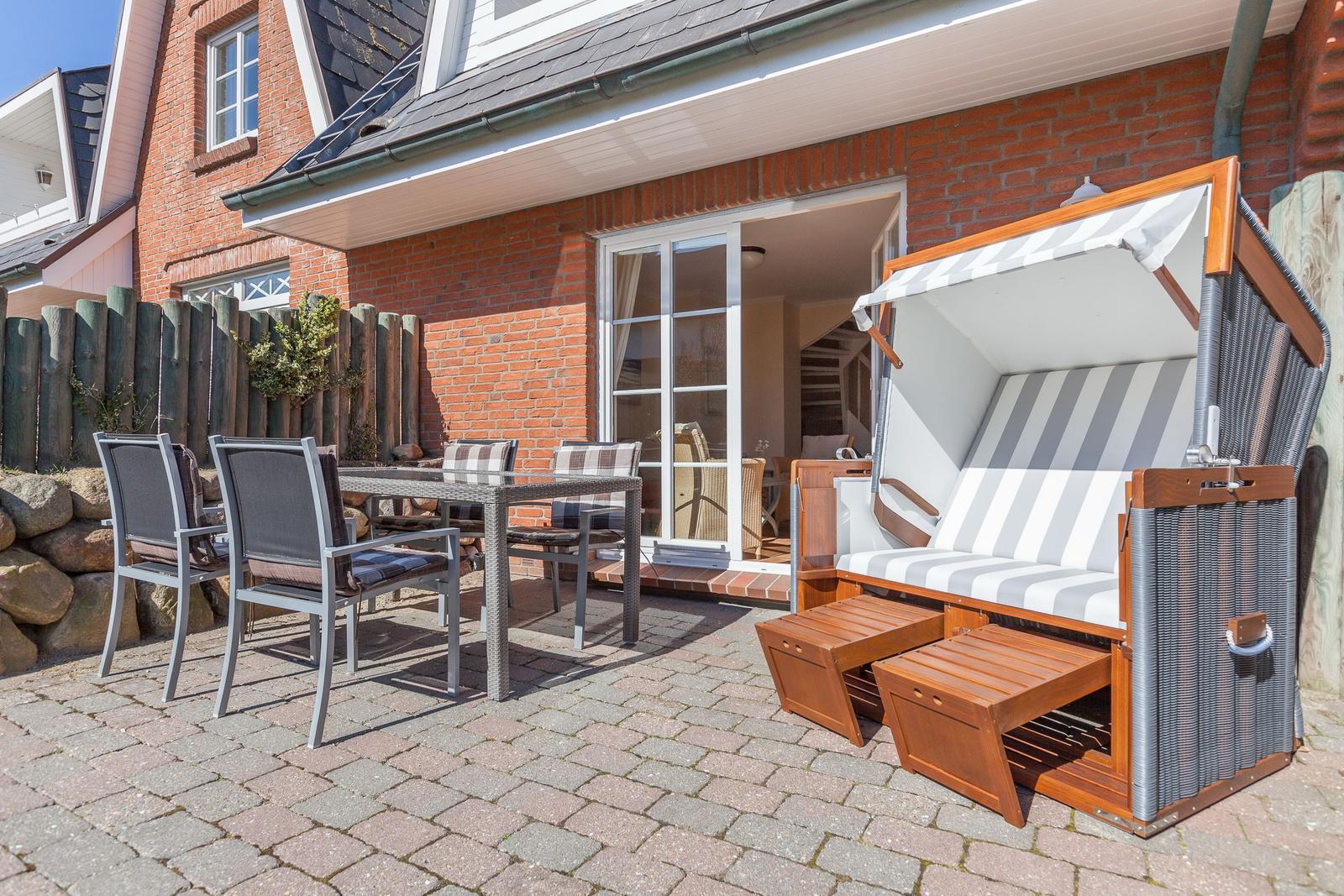 Terrasse mit Gartenmöbeln und Strandkorb vor einem Haus mit Backsteinfassade.