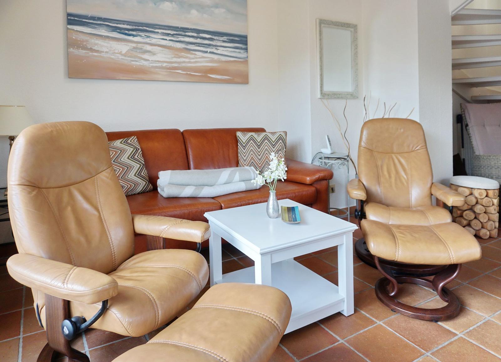 Lounge mit zwei Ledersessel, Sofa und Tisch. Wandbild zeigt Strand.