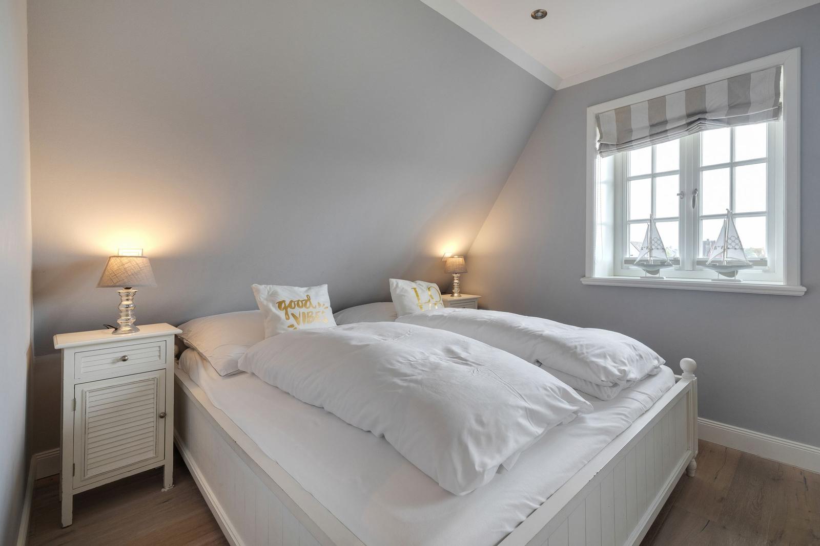 Schlafzimmer mit Doppelbett, Nachttisch und Fenster mit Segelbooten.