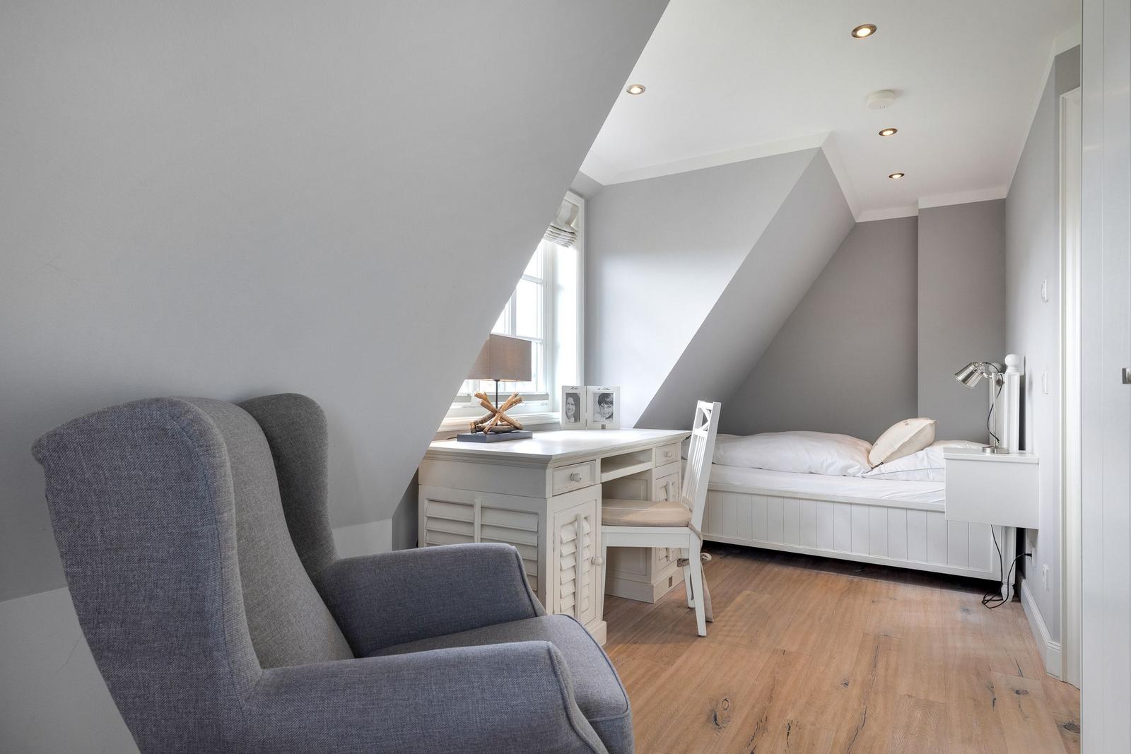 Schlafzimmer mit Dachschräge, Bett, Schreibtisch und Sessel.
