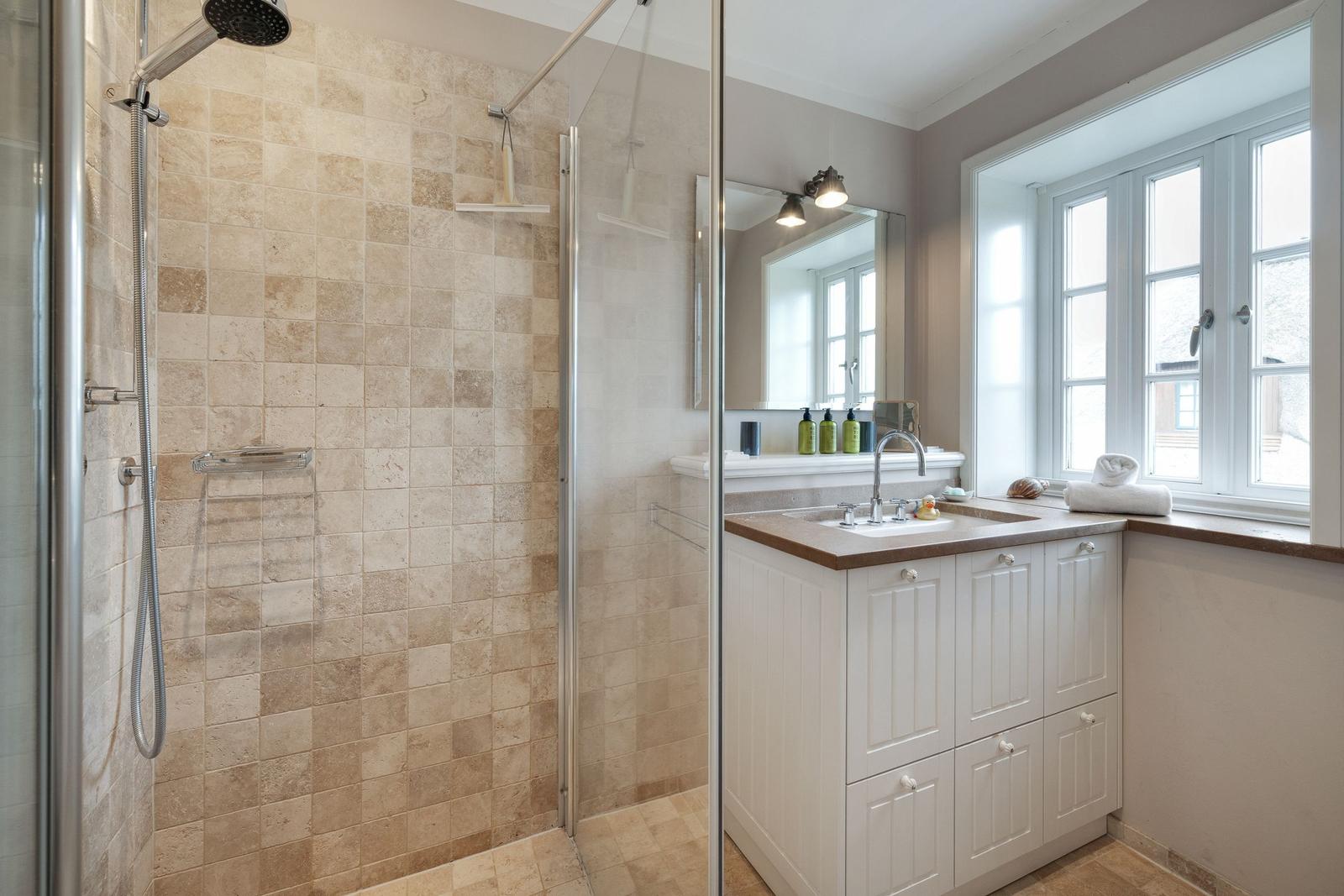 Dusche mit Duschbrause und Waschbecken mit Spiegel und Fenster