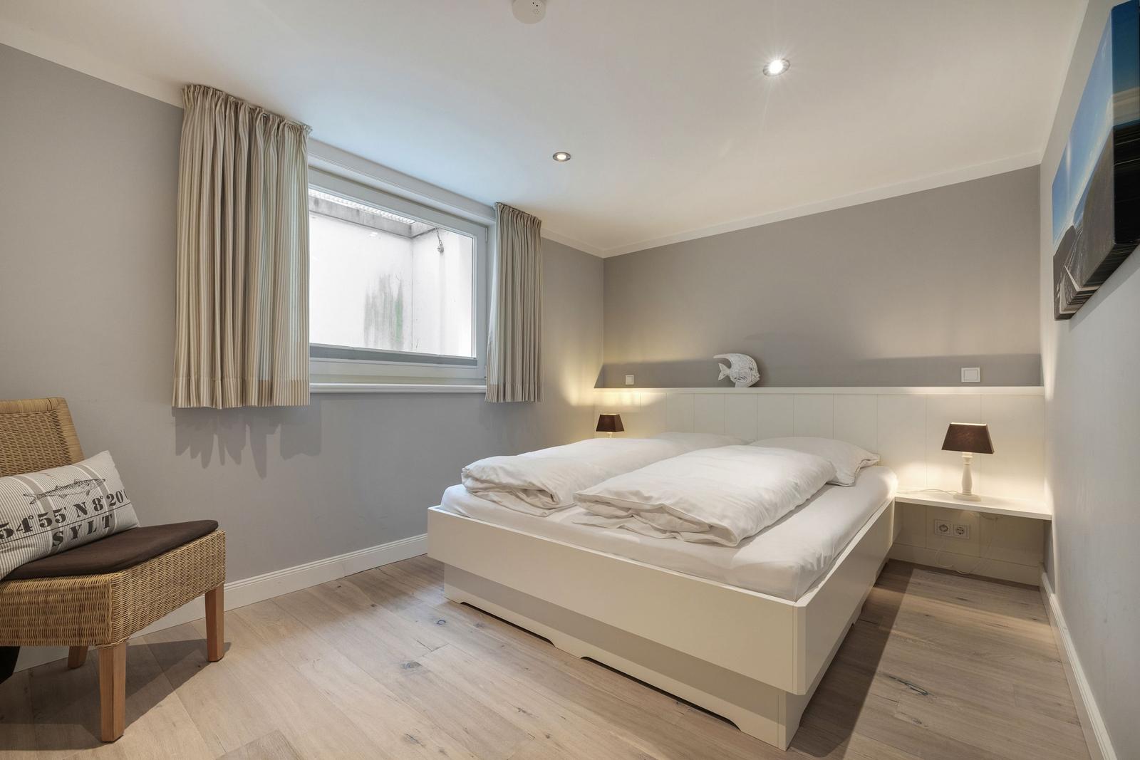 Schlafzimmer mit weißem Bett, Holzboden und Fenster mit Vorhängen.