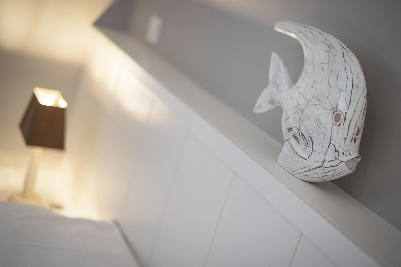 Ein weißes Fischdekoration steht auf einem weißen Kopfteil neben einer Lampe.