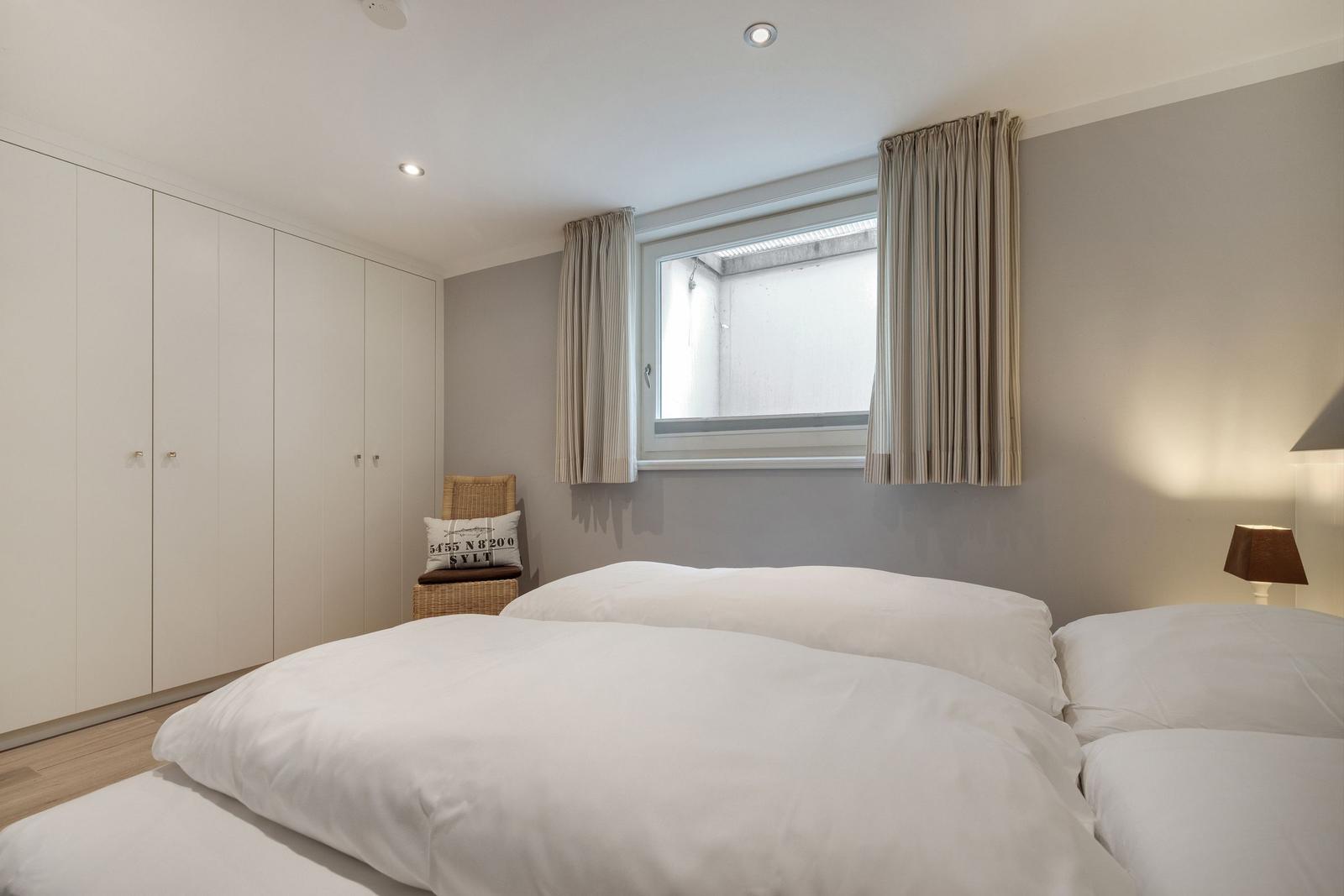 Schlafzimmer mit Doppelbett, Kleiderschrank und Fenster mit Vorhängen.