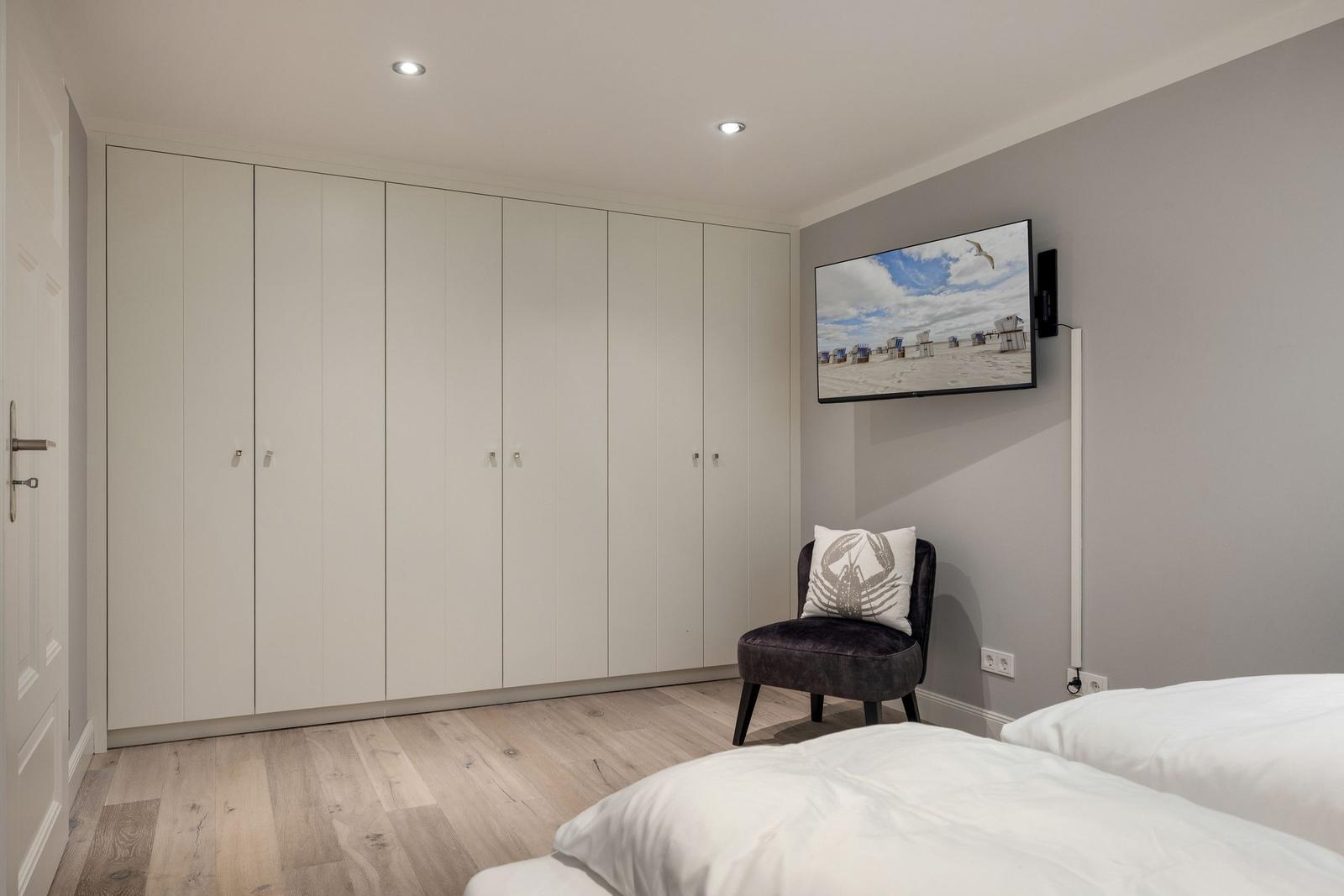 Schlafzimmer mit weißem Kleiderschrank, Bett und Wandfernseher.