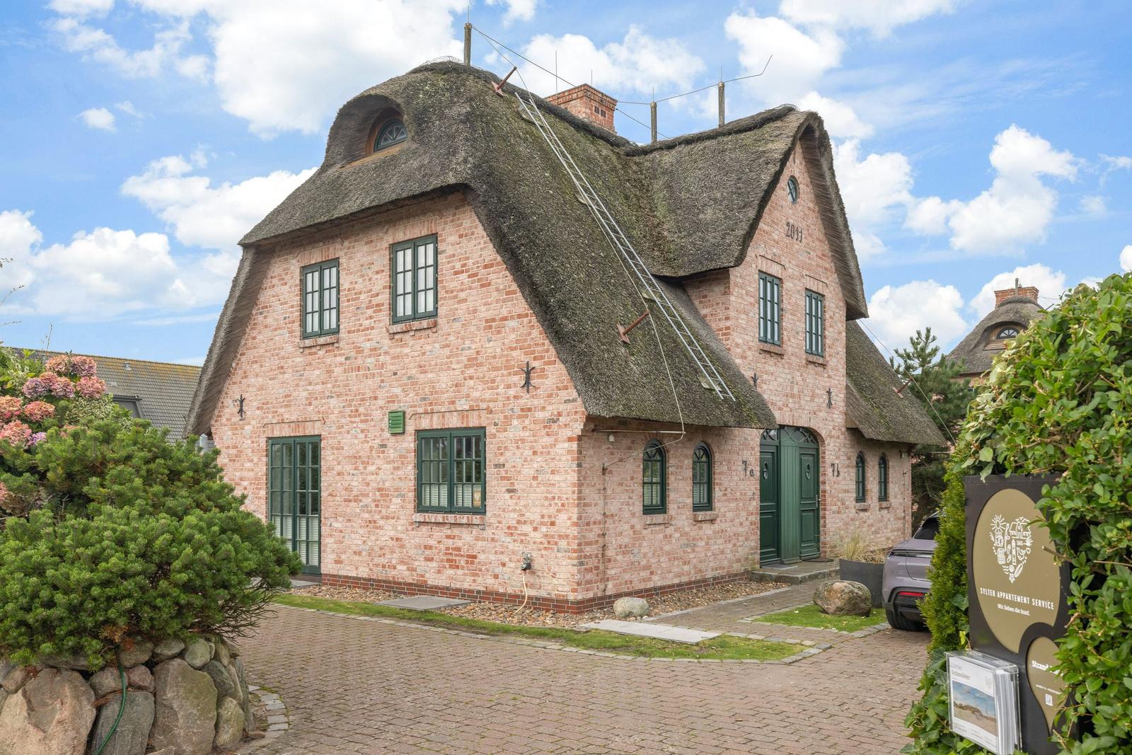 Rotes Backsteinhaus mit Strohdach und grünen Fenstern. Vorhof mit Kies und Pflanzen.