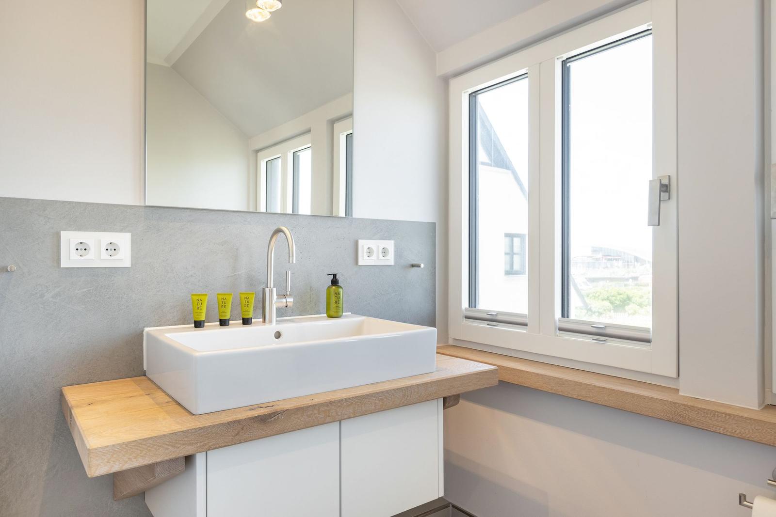 Bathroom with sink, mirror, and window. Wooden surface and gray wall.
