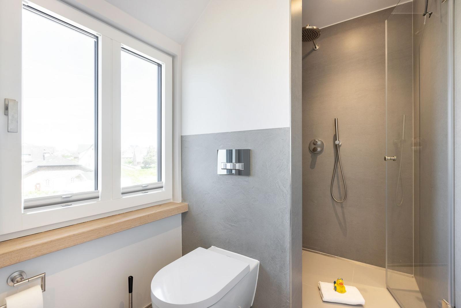Bathroom with shower, toilet, and window with view.