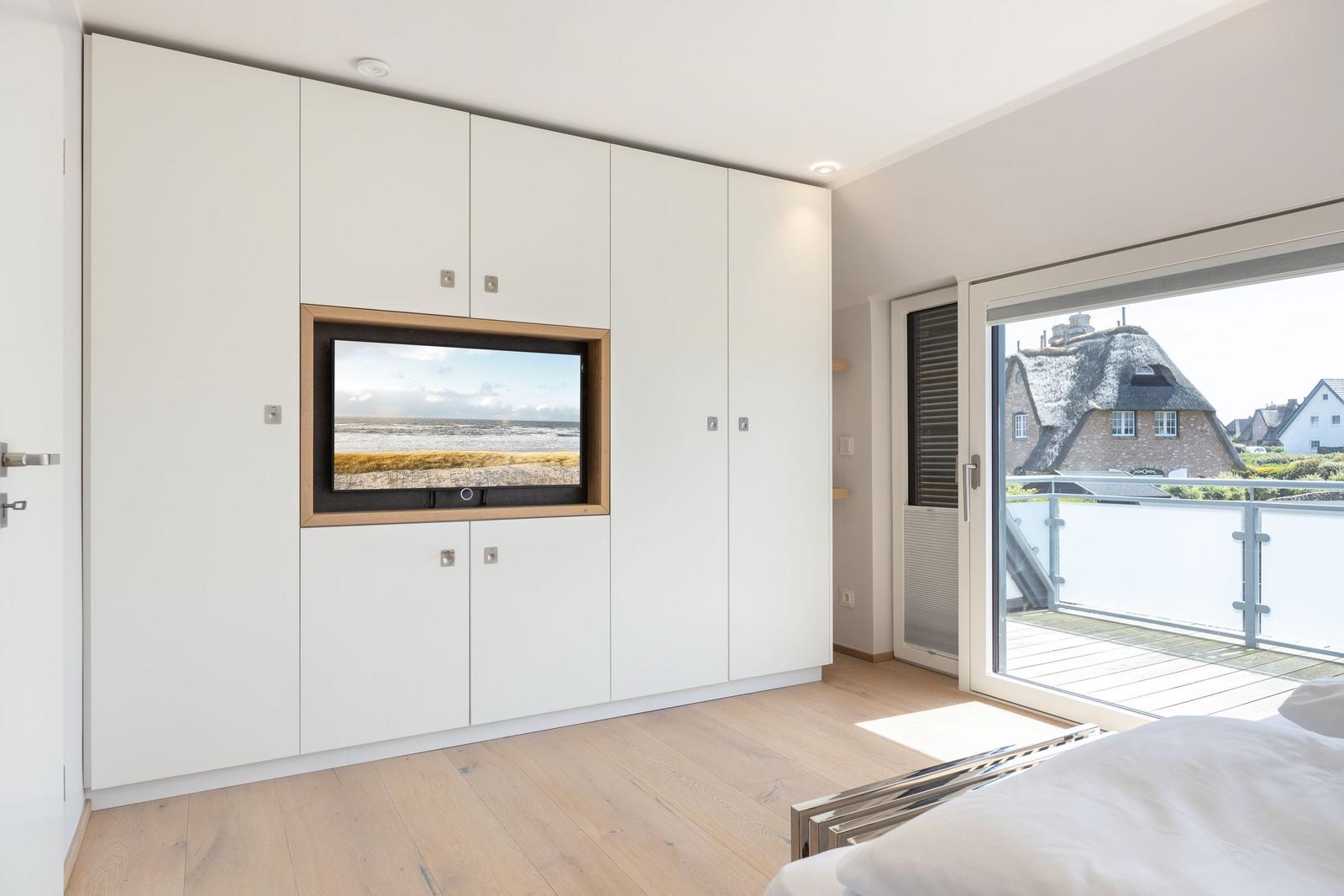 Bedroom with TV in wall and balcony view of thatched roof house