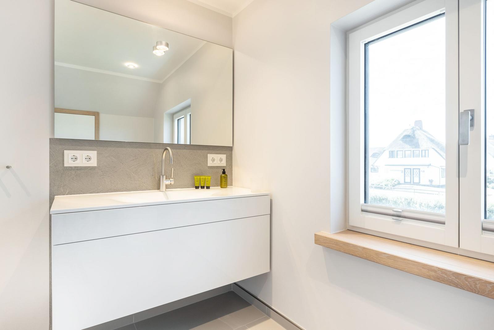 Bathroom with sink, mirror, and window with view of house.
