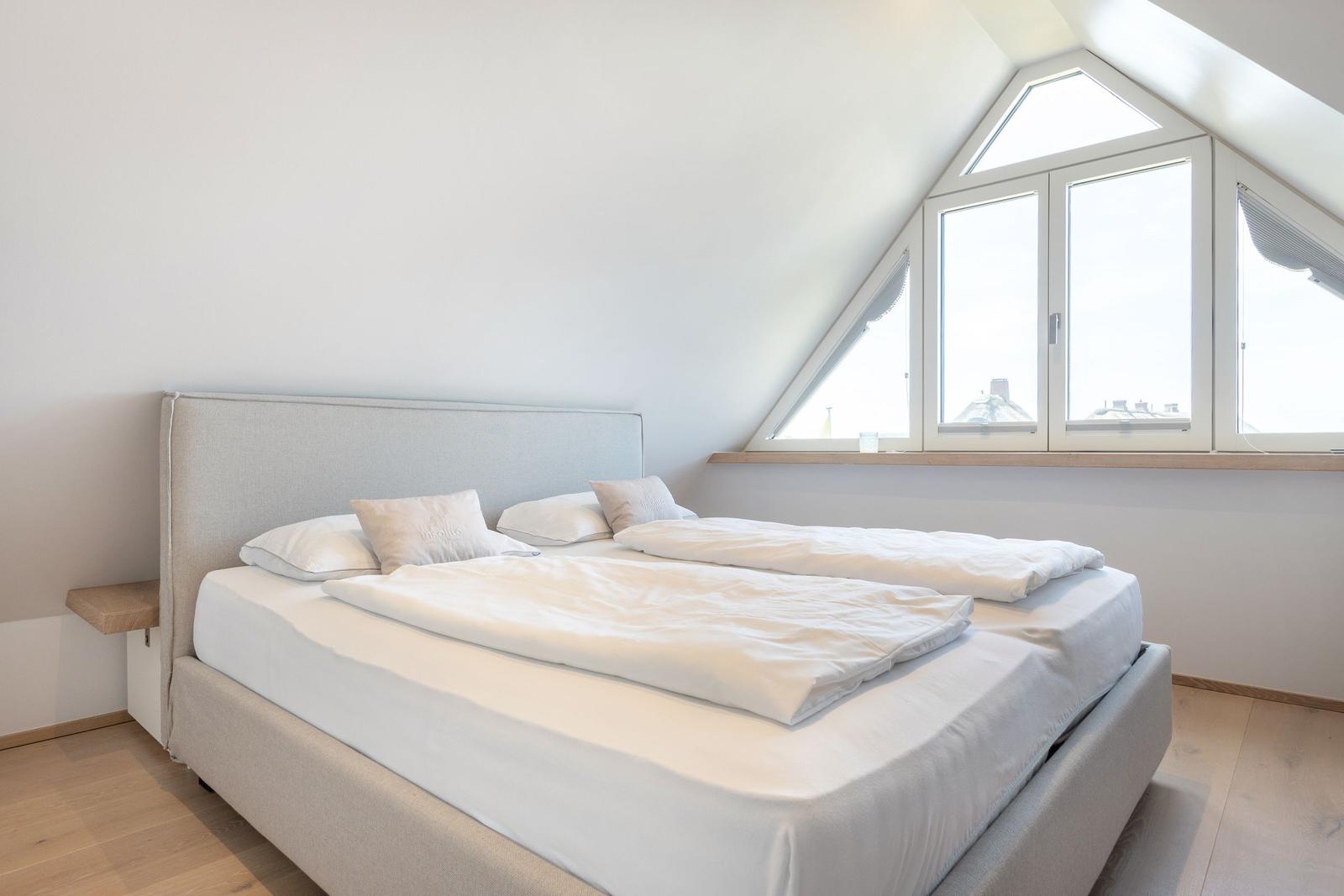 Double bed with white bedding under a skylight window.