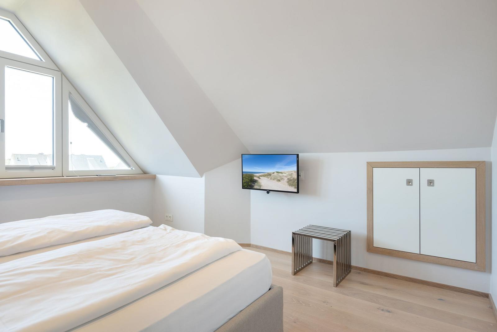 Bedroom with sloped ceiling, bed, TV, and wardrobe.