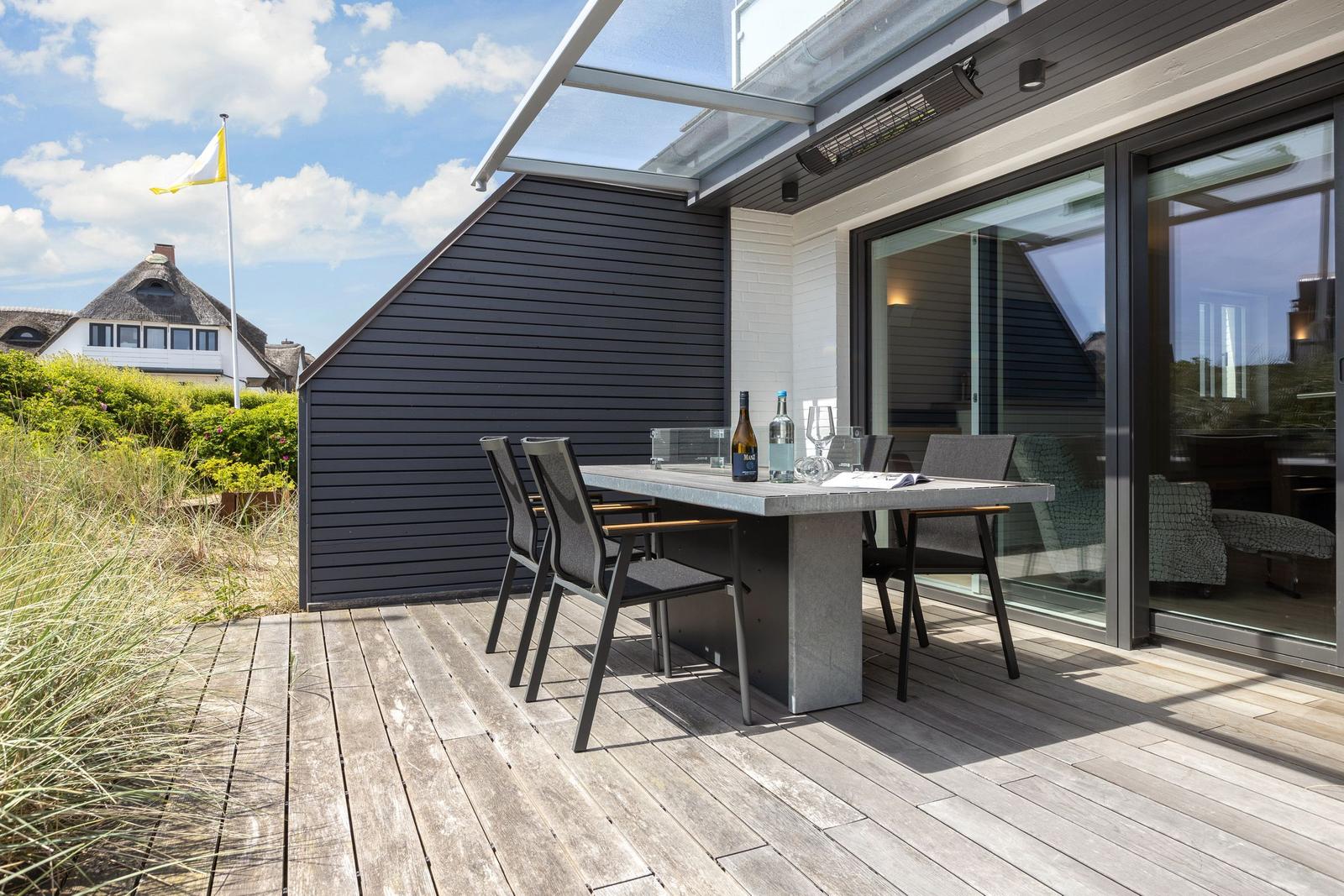 Terrace with table and chairs, modern house with glass facade and wooden deck.
