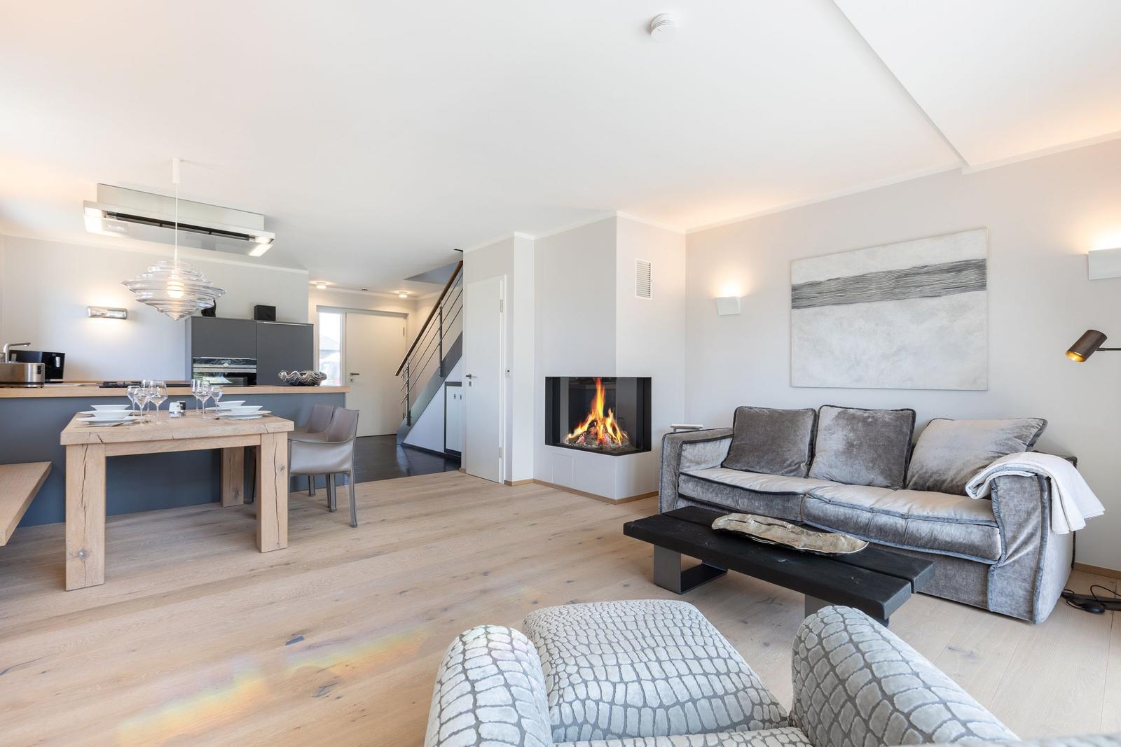 Living room with fireplace, sofa, and dining table. Kitchen in background.