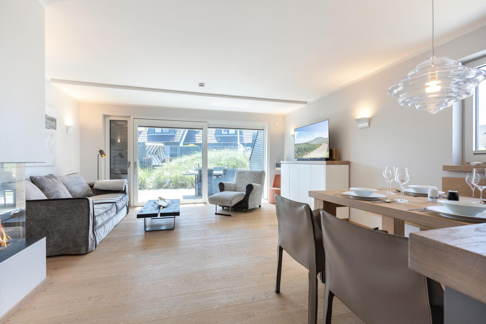 Living and dining area with wooden floor, sofa, TV, and table with chairs.