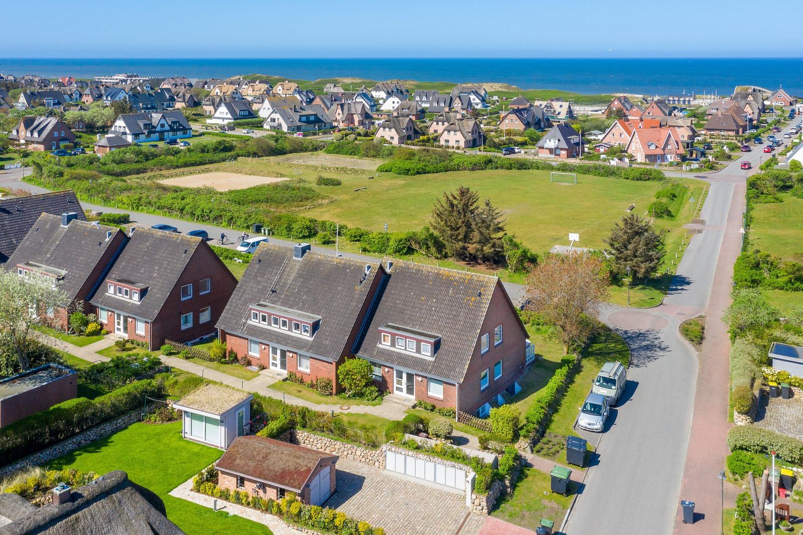 Village with houses, green areas, and sea in the background.