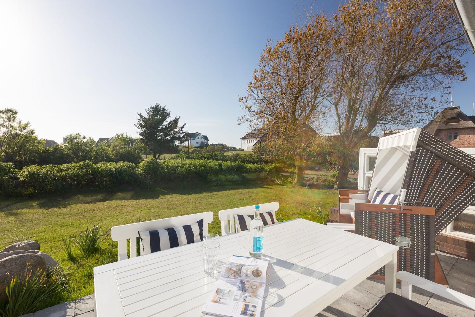 White table with chairs and lounge chair on terrace with view of lawn and trees.
