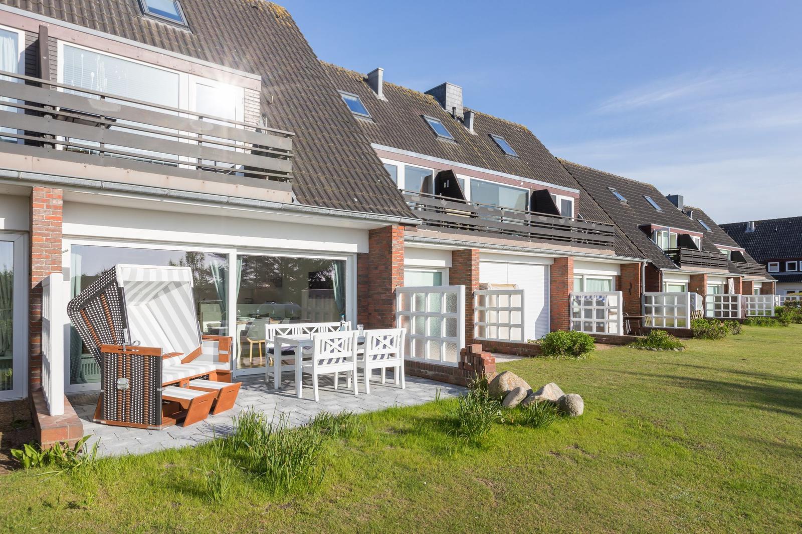 Terrace with table, chairs, and beach chair. Modern house with balcony and garden.