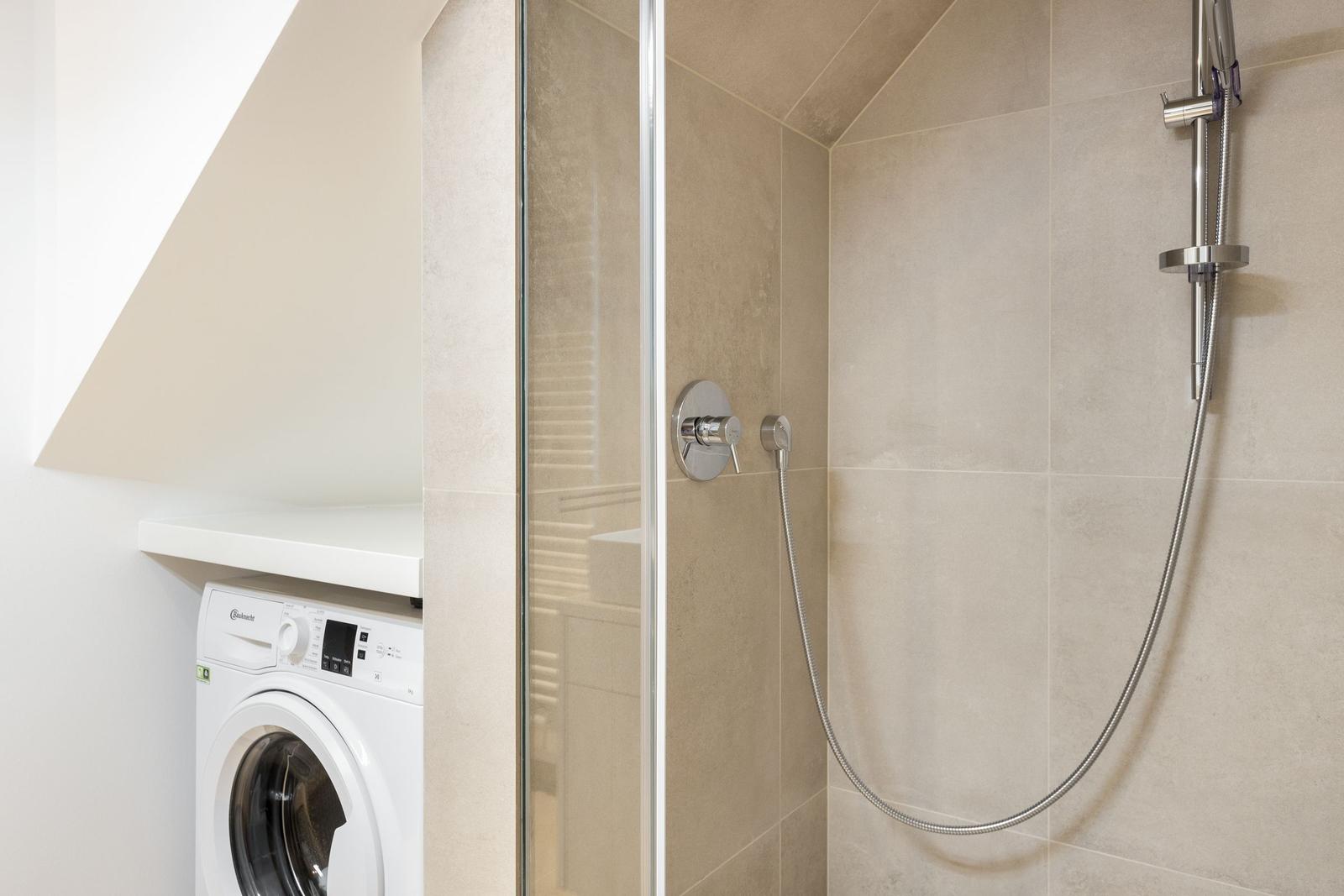 Shower with glass enclosure and washing machine in bathroom