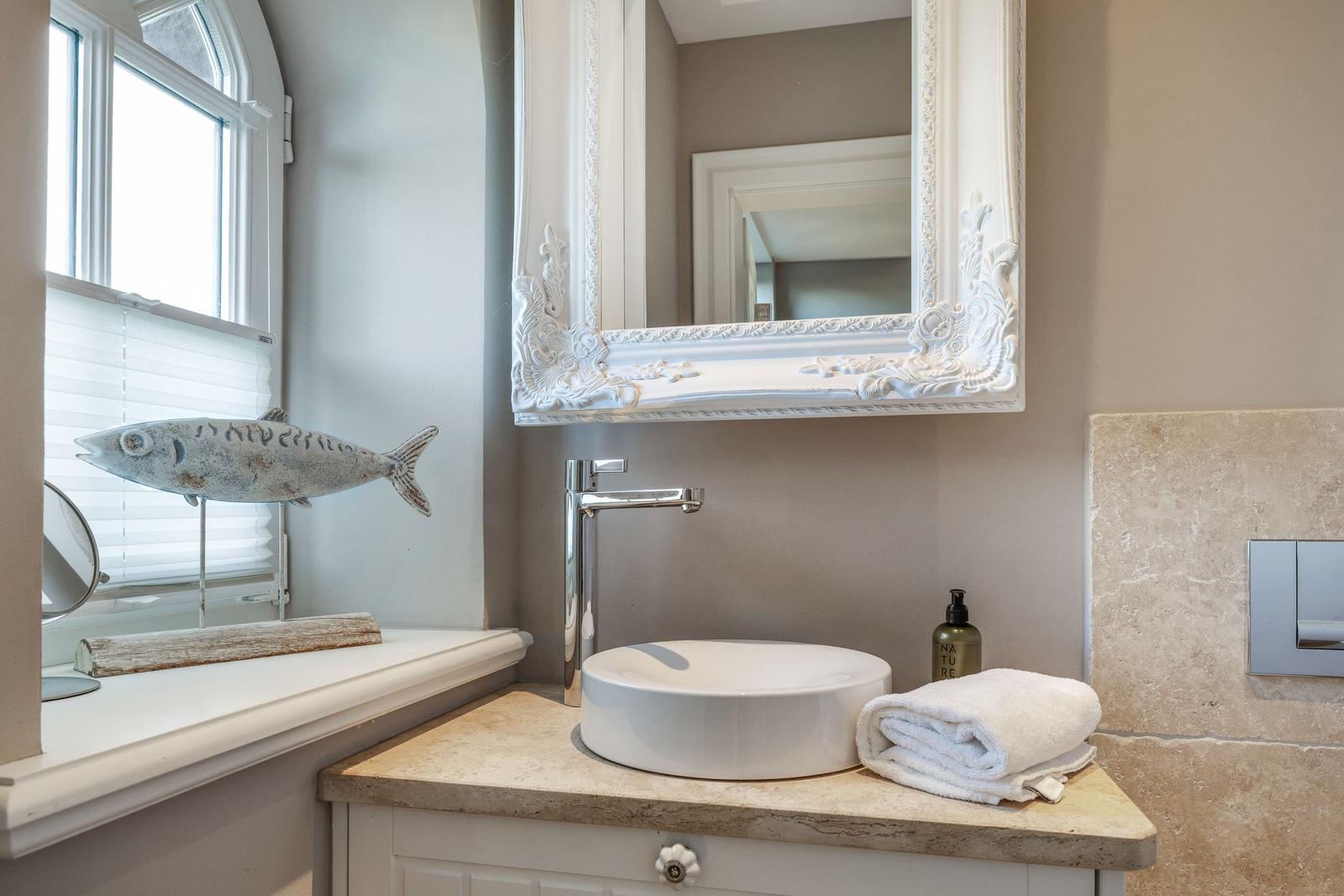 Badezimmer mit Waschtisch, Spiegel und Fenster. Dekoration: Fischfigur und Handtuch.