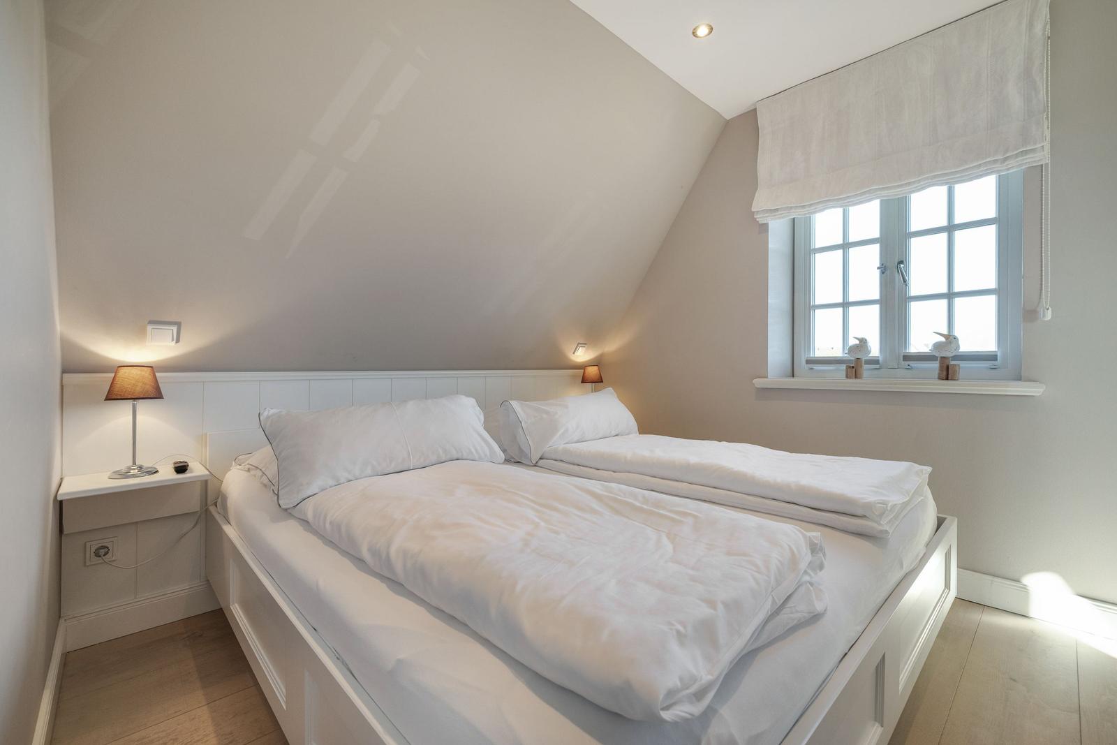 Schlafzimmer mit Doppelbett, Fenster und Nachttisch.