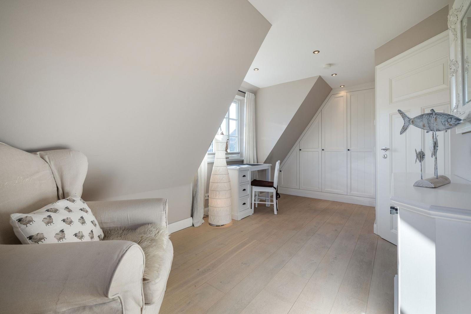 Schlafzimmer mit Schreibtisch, Kleiderschrank und Sofa unter Dachschrägen.