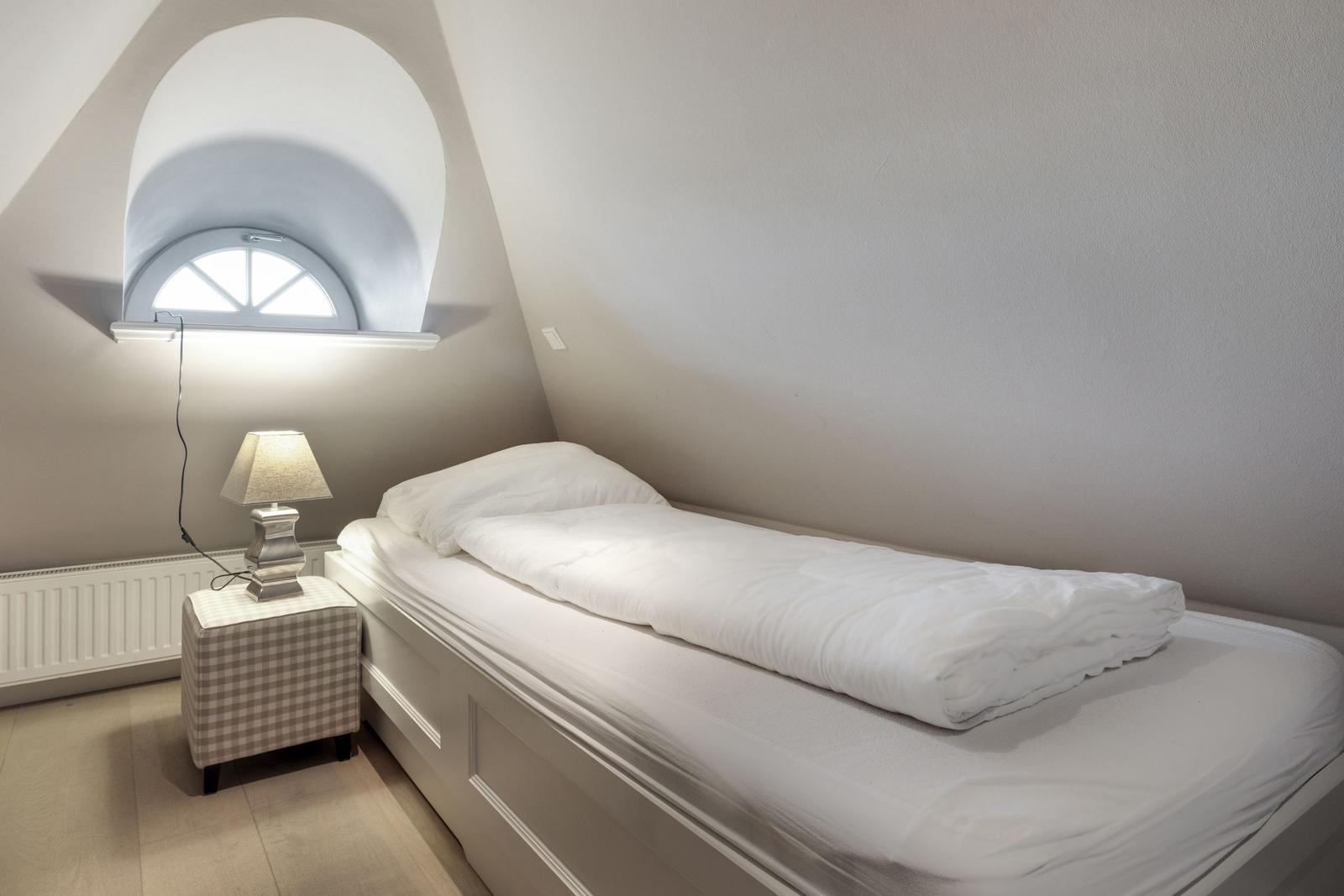Schlafzimmer mit Bett, Nachttisch und Bogenfenster.