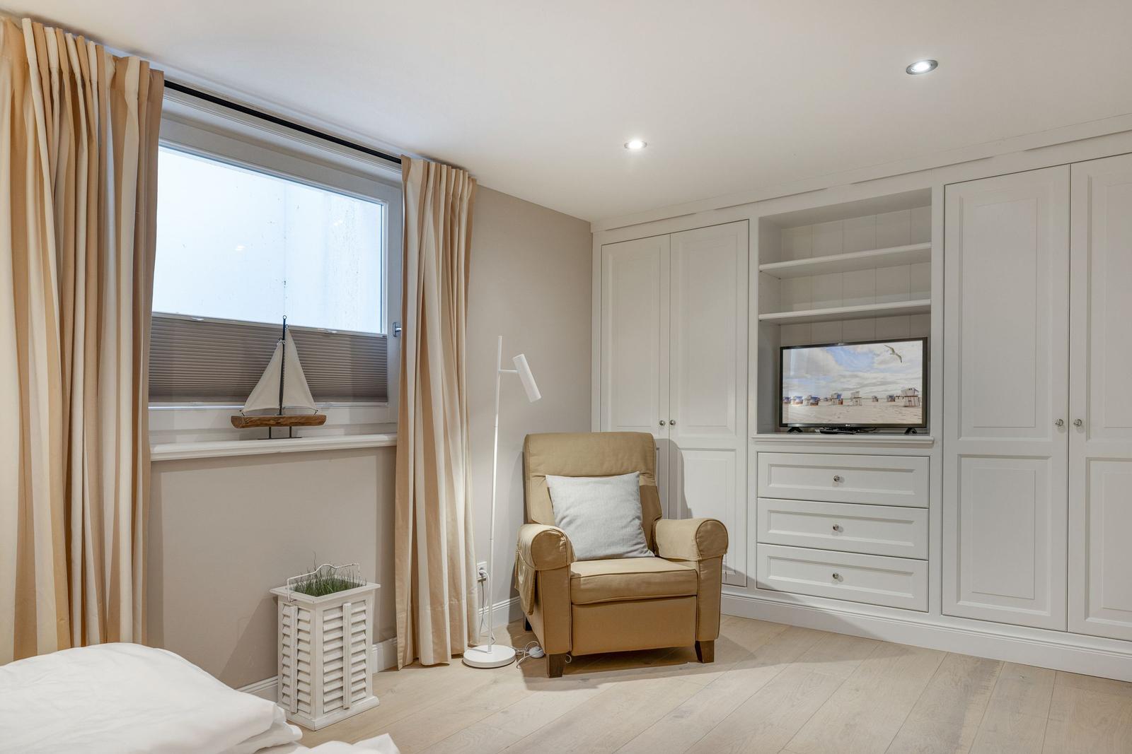 Ein Schlafzimmer mit Bett, Sessel, TV und Fenster mit Segelboot.
