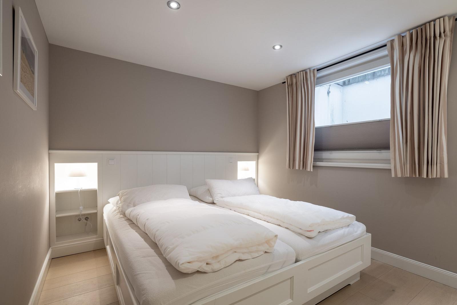 Schlafzimmer mit Doppelbett, Fenster und Nachttischen.