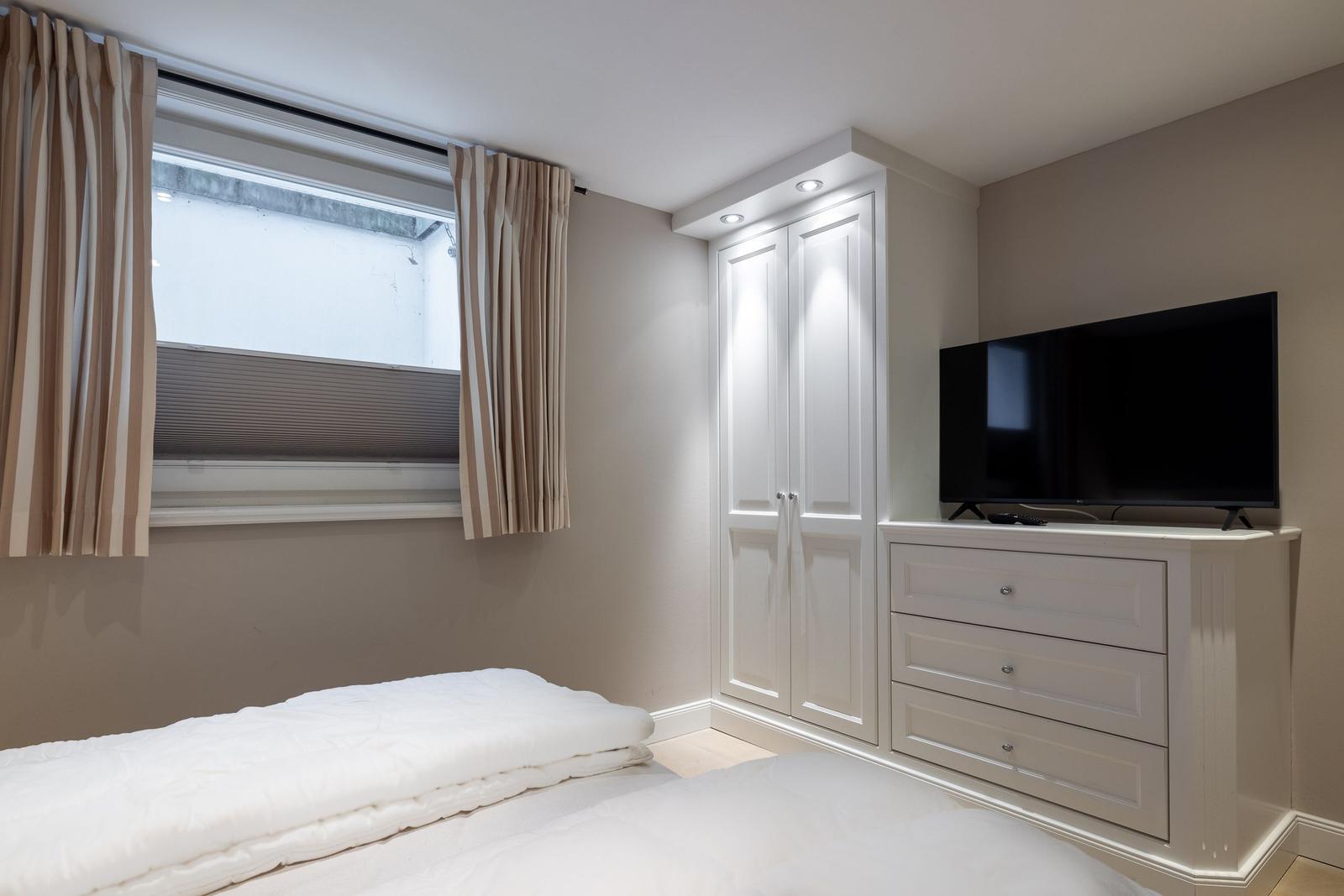 Schlafzimmer mit weißem Bett, Kleiderschrank und Fernseher.