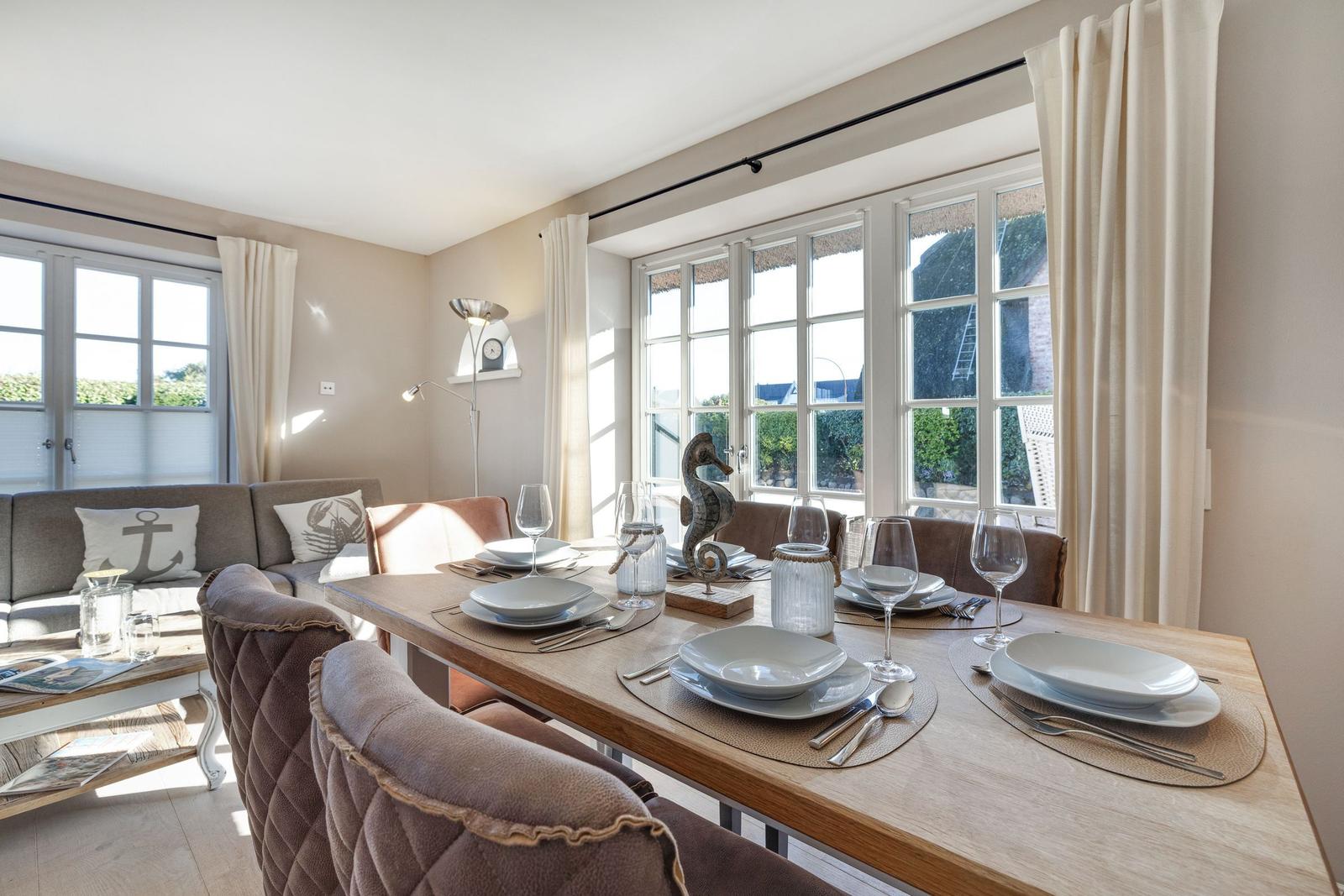 Esszimmer mit Tisch, Stühlen und Fenstern. Anrichten und Dekoration sind sichtbar.
