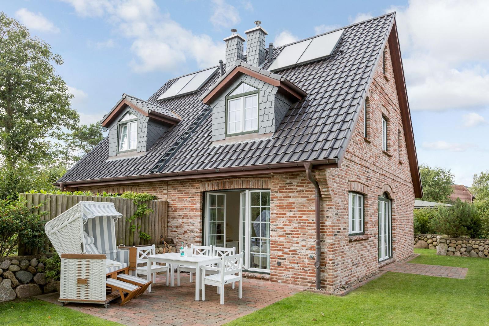 Haus mit Terrasse, weißem Tisch und Stühlen, Strandkorb und grünem Rasen.