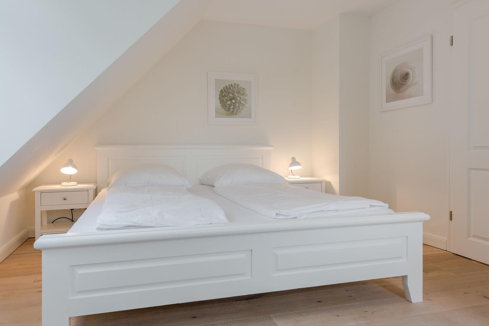 Schlafzimmer mit weißem Bett, zwei Nachttischen und Bildern an der Wand.