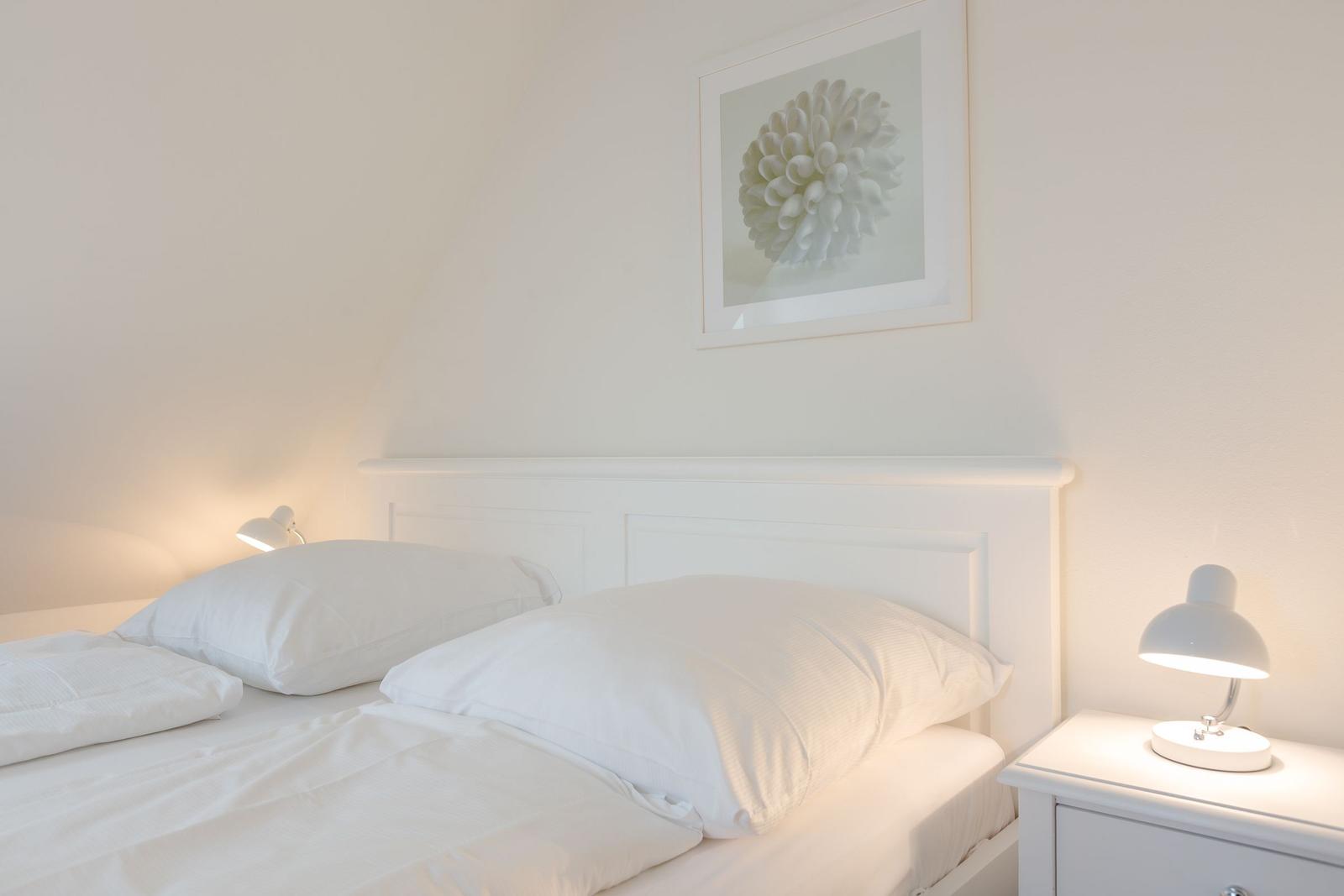Schlafzimmer mit weißem Bett, Nachttisch und Wandbild.