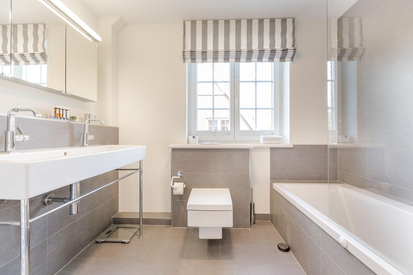 Badezimmer mit Badewanne, WC und Waschbecken unter Fenster