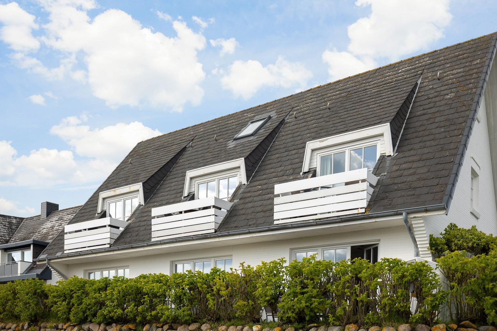 House with dormer windows and white balconies under blue sky.