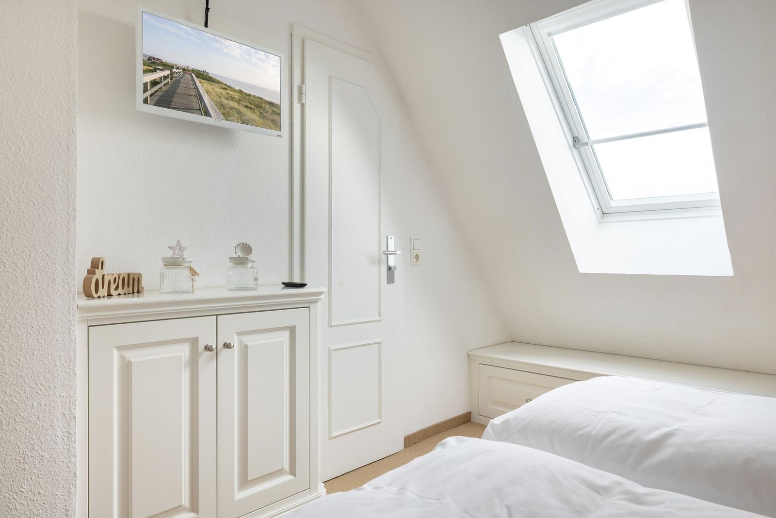 Bedroom with sloped ceiling, skylight, bed, and cabinet. TV mounted on wall.
