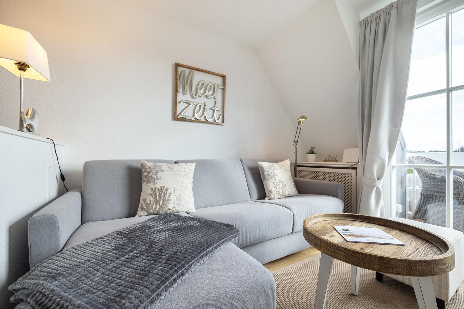 Living room with gray sofa, wooden table, and window to terrace.