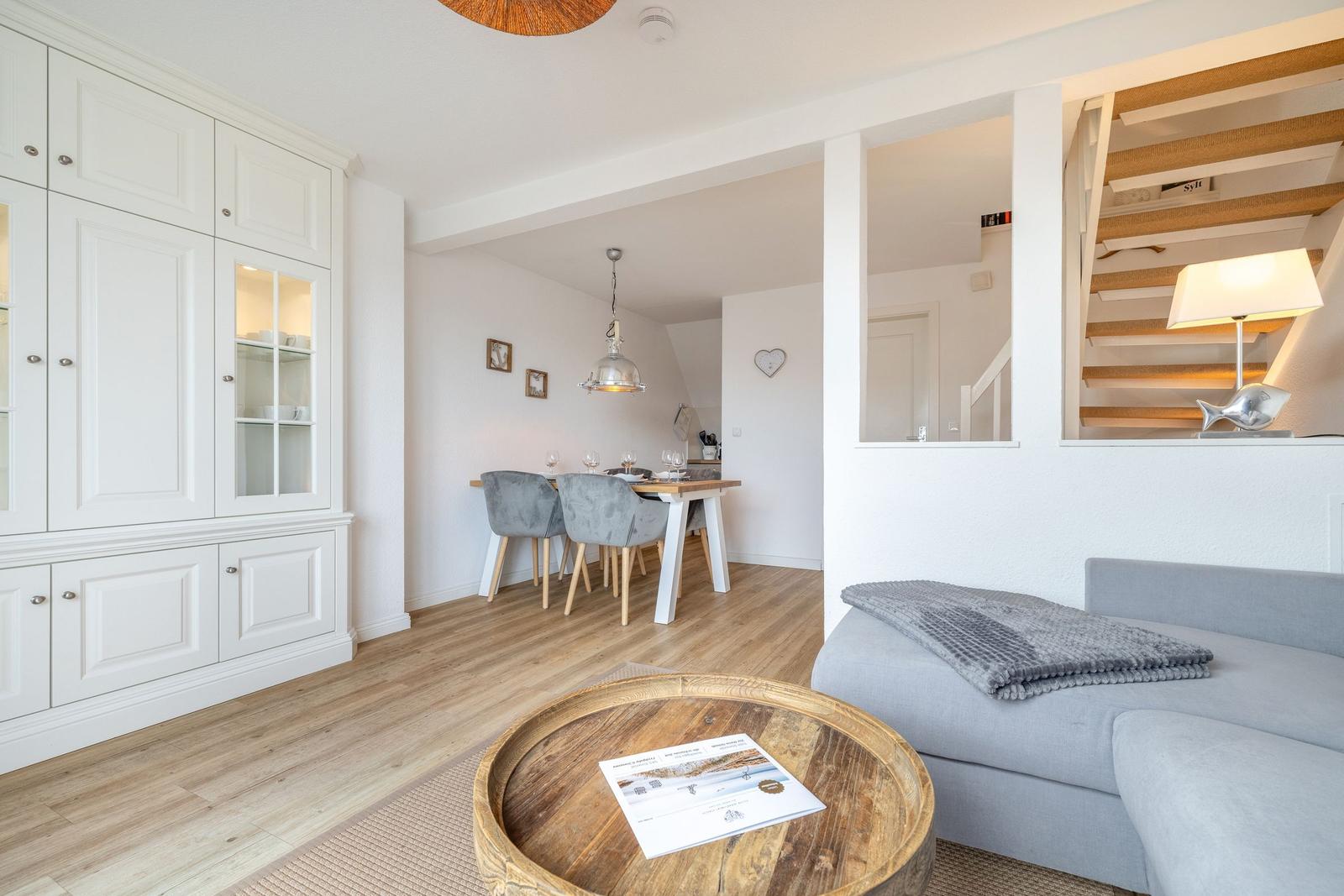 Living and dining area with wooden floor, sofa, and kitchen cabinets.